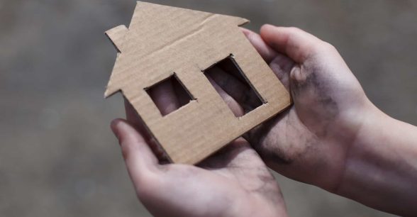 A pair of hands holding a cardboard cutout of a house