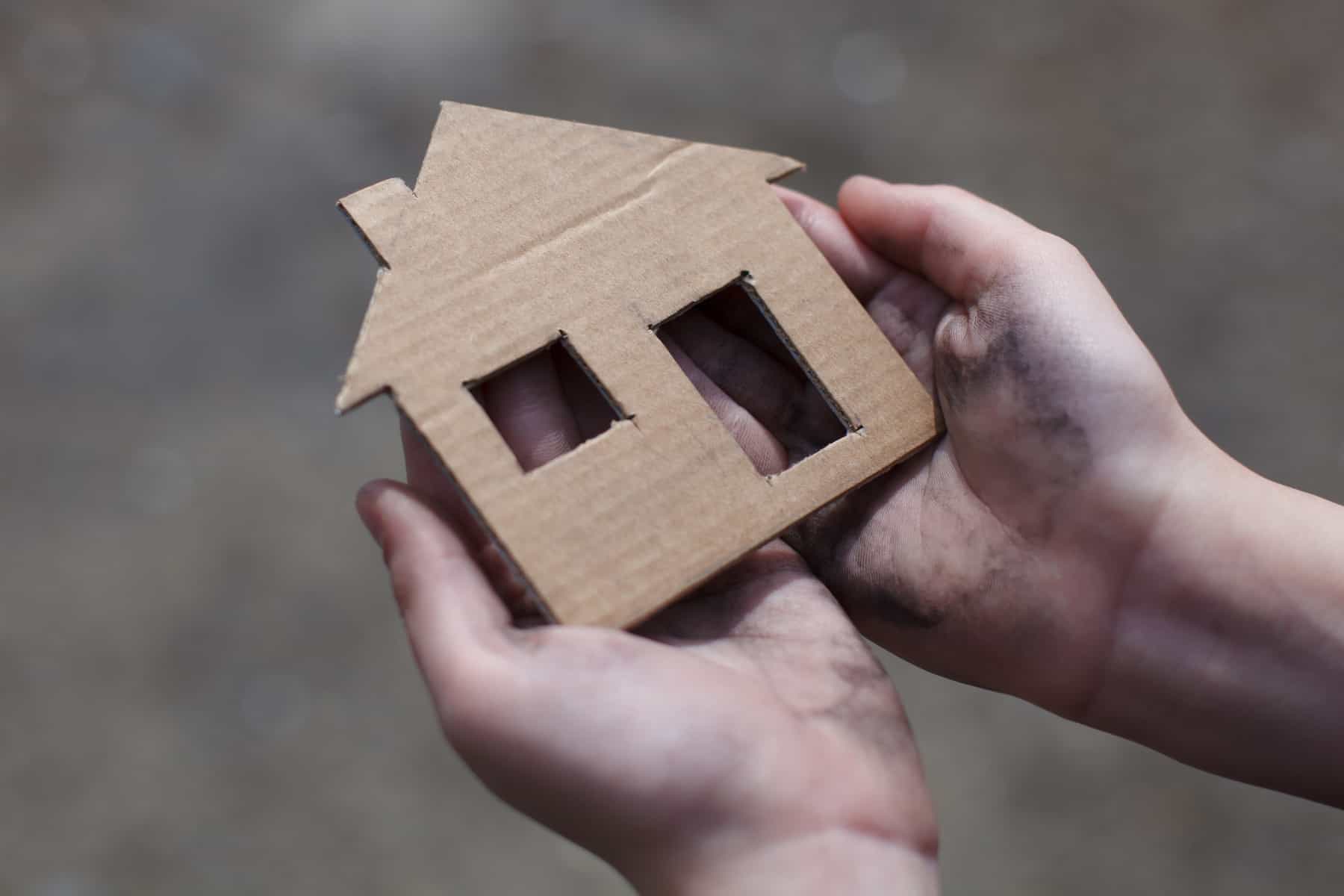 A pair of hands holding a cardboard cutout of a house