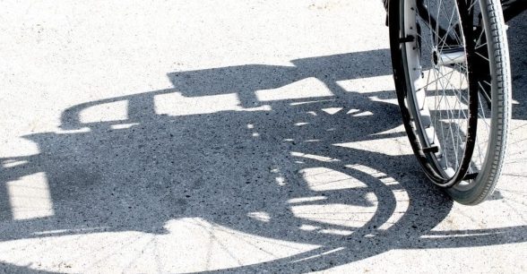 Side of a wheelchair, mainly the wheel, giving off a shadow of the wheelchair on the ground.