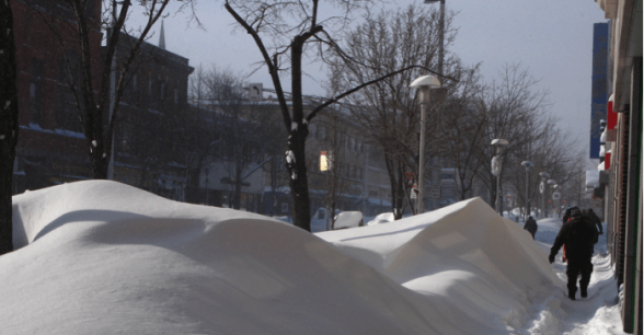 A large snow drift covering a sidewalk, making it impassable.
