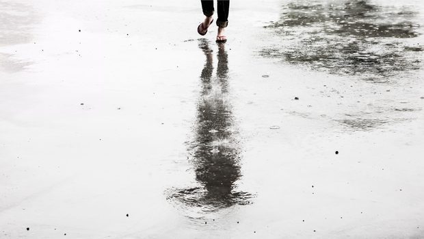 Person looking at their reflection on pavement that is wet. You can only see the actual person's feet. They are wearing flip-flops.