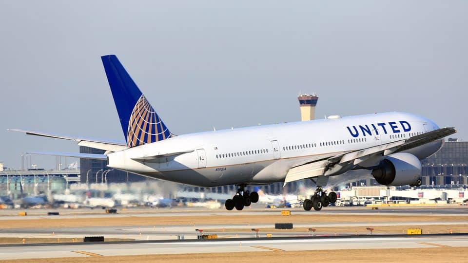 A United airplane hovering over a runway during the daytime.