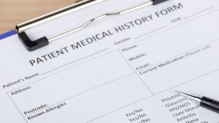 Photo of a blank patient medical history form on a clipboard with a pen resting on top of it.