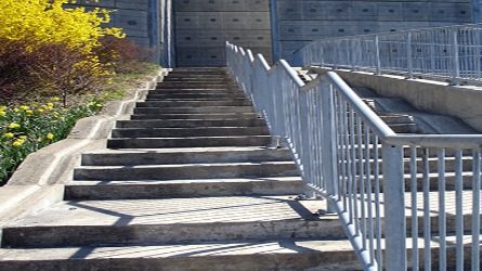 A wide cement staircase outside with a big metal railing in the middle.