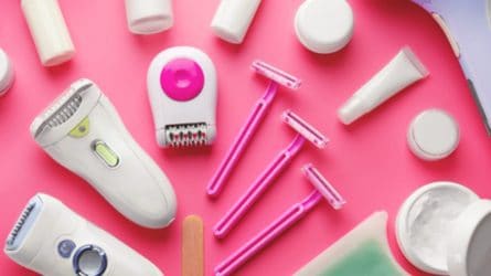 Assorted pink and white hair removal tools, such a razors and electric shavers, on a pink background.