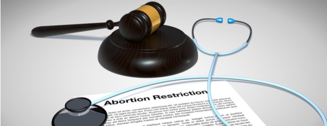 A paper that is titled "abortion restriction rests on a table, with a stethoscope draped across it and a gavel next to it.