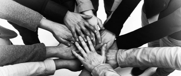 A black and white photo of hands of different skin tones piled together in a circle showing solidarity.