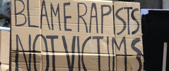 A cardboard sign being held up. The sign says "blame rapists, not victims."