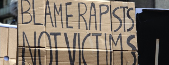 A cardboard sign being held up. The sign says "blame rapists, not victims."