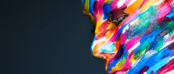 A photo of a person whose face is painted with lines in a rainbow of colors