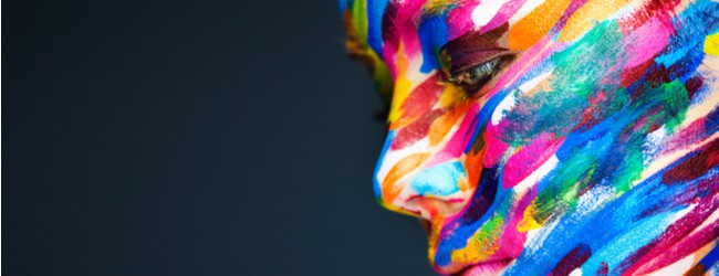 A photo of a person whose face is painted with lines in a rainbow of colors