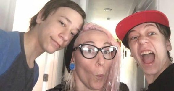 Photo of Maggie Winston, a white woman with light pink hair and glasses, in between her two sons, both teenage.