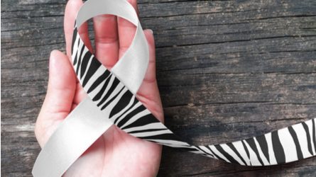 A hand resting on a wooden surface holding a zebra-print awareness ribbon.