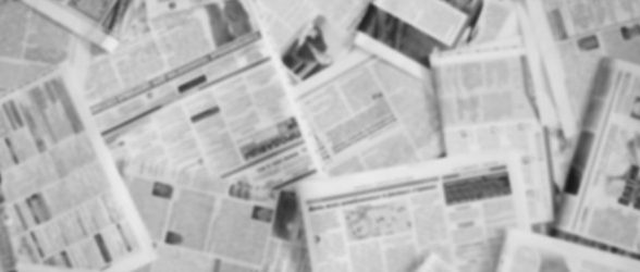 A pile of newspapers spread out over one another. The text is blurred and unreadable.