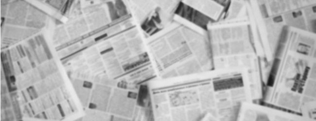 A pile of newspapers spread out over one another. The text is blurred and unreadable.