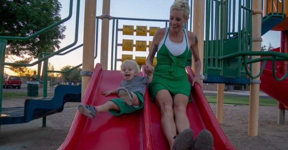 A photo of Anna and her toddler son going down a big red slide together.