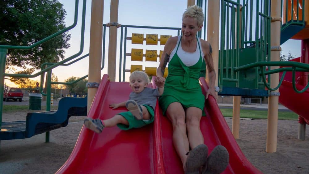 A photo of Anna and her toddler son going down a big red slide together.