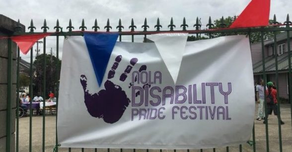 Sign with a handprint that reads "NOLA Disability Pride Festival" hanging on a wrought iron gate.