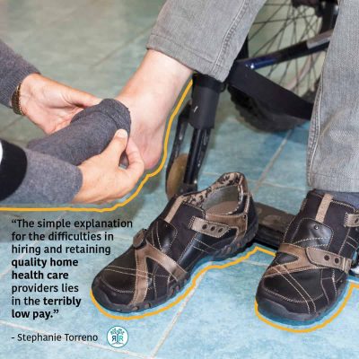 Quote from Stephanie Torreno: "The simple explanation for the difficulties in hiring and retaining quality home health care providers lies in the terribly low pay." Photo showing a person kneeling down, assisting a person sitting in a wheelchair with putting on a sock.