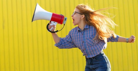 A woman is yelling into a megaphone, in an empowered pose.
