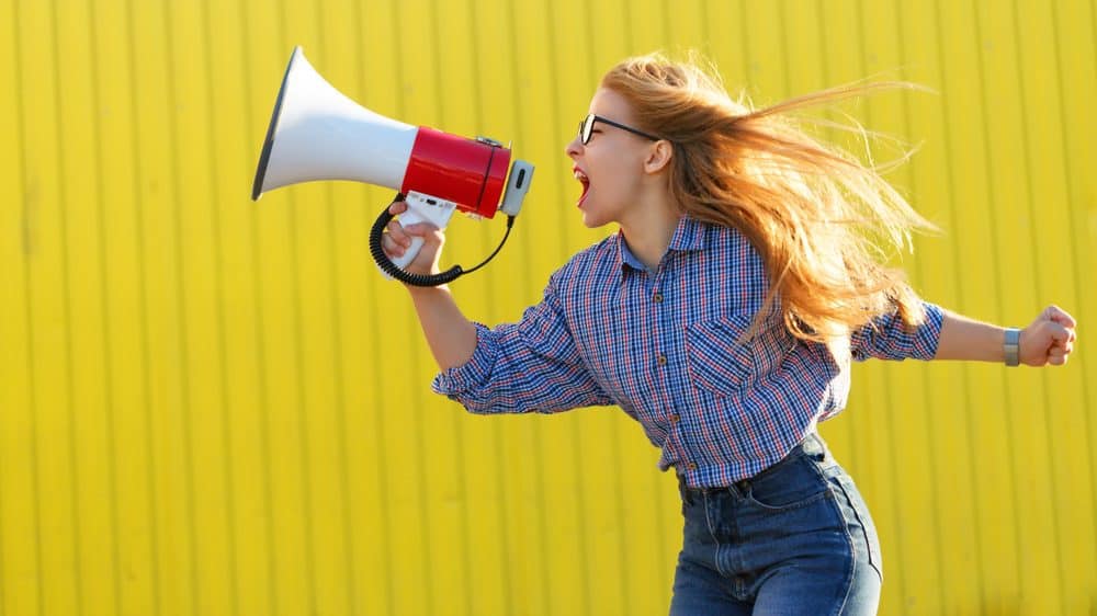 A woman is yelling into a megaphone, in an empowered pose.