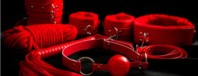Red leather BDSM accessories including ball gag, cuffs, rope, flogger, collar and leash.