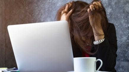Woman sitting at her laptop with her head in her hands and her hair over her face.