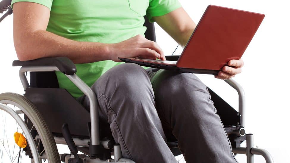 A person in a manual wheelchair holds a red laptop in their lap.