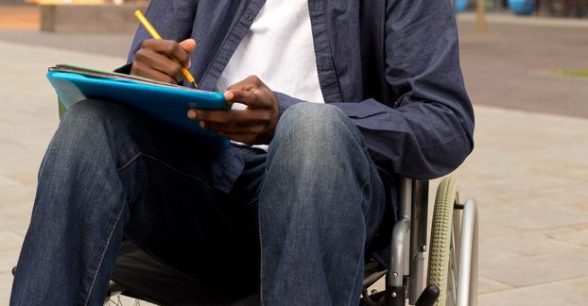 A person in a wheelchair holding folders and a pen