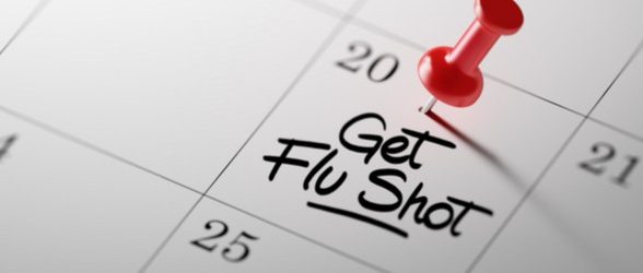 Image of a calendar with the words "get flu shot" written down in the box for the 20th. There is a red push pin on top of it.