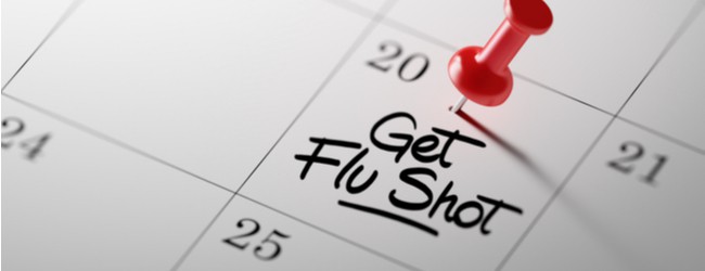 Image of a calendar with the words "get flu shot" written down in the box for the 20th. There is a red push pin on top of it.