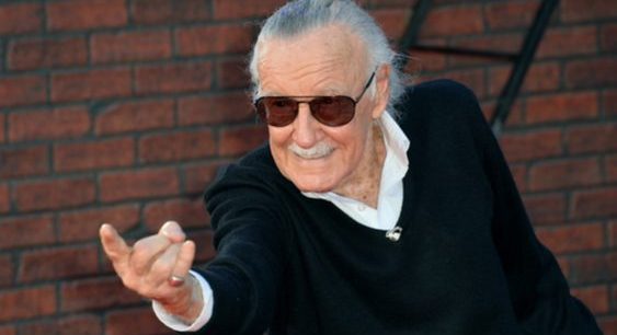 Photo of Stan Lee in a black suit and sunglasses, pointing his finger forward.