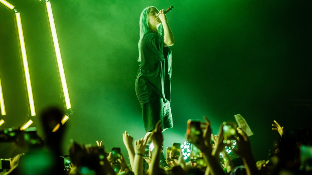 green toned photo of Billie Eilish singing on stage to a crowd