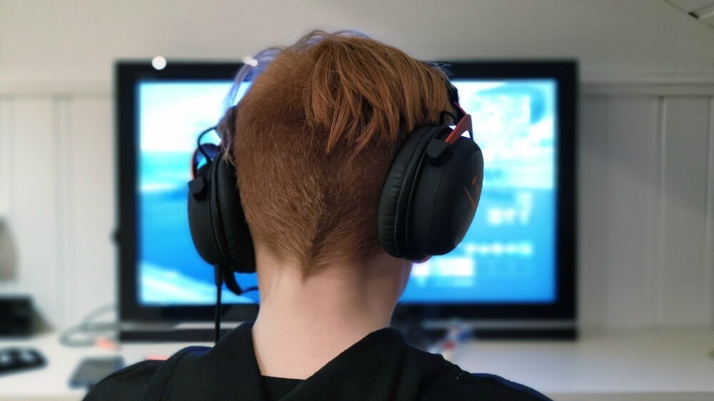 Photo of person wearing headphones and a sweatshirt, sitting in front of a computer screen