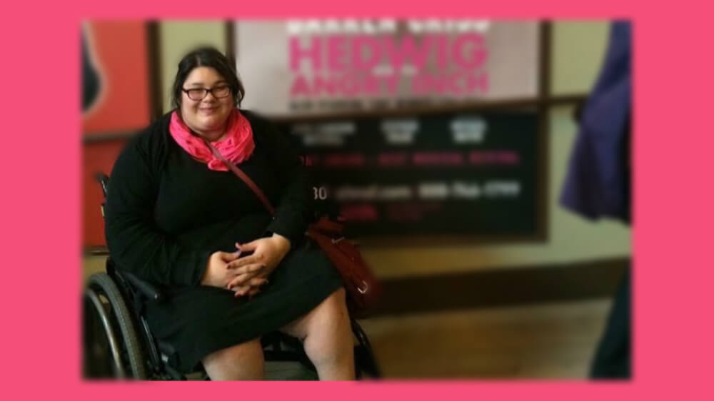 Photo of Yolanda in a black dress and pink scarf sitting in a manual wheelchair