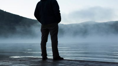 A person standing alone, looking out onto a hazy lake.