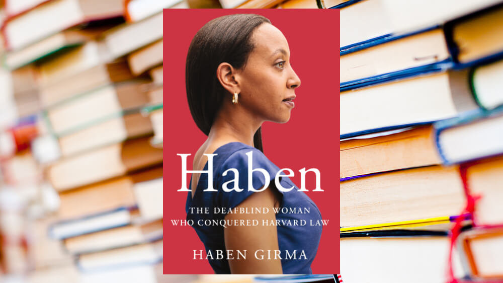 A photo of Haben Girma's book cover positioned over a background of piles of books.