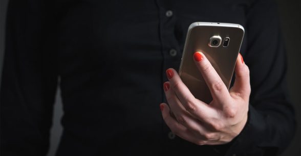 Photo of a person with red-painted fingernails holding a smartphone. On the person's torso/hand is showing.