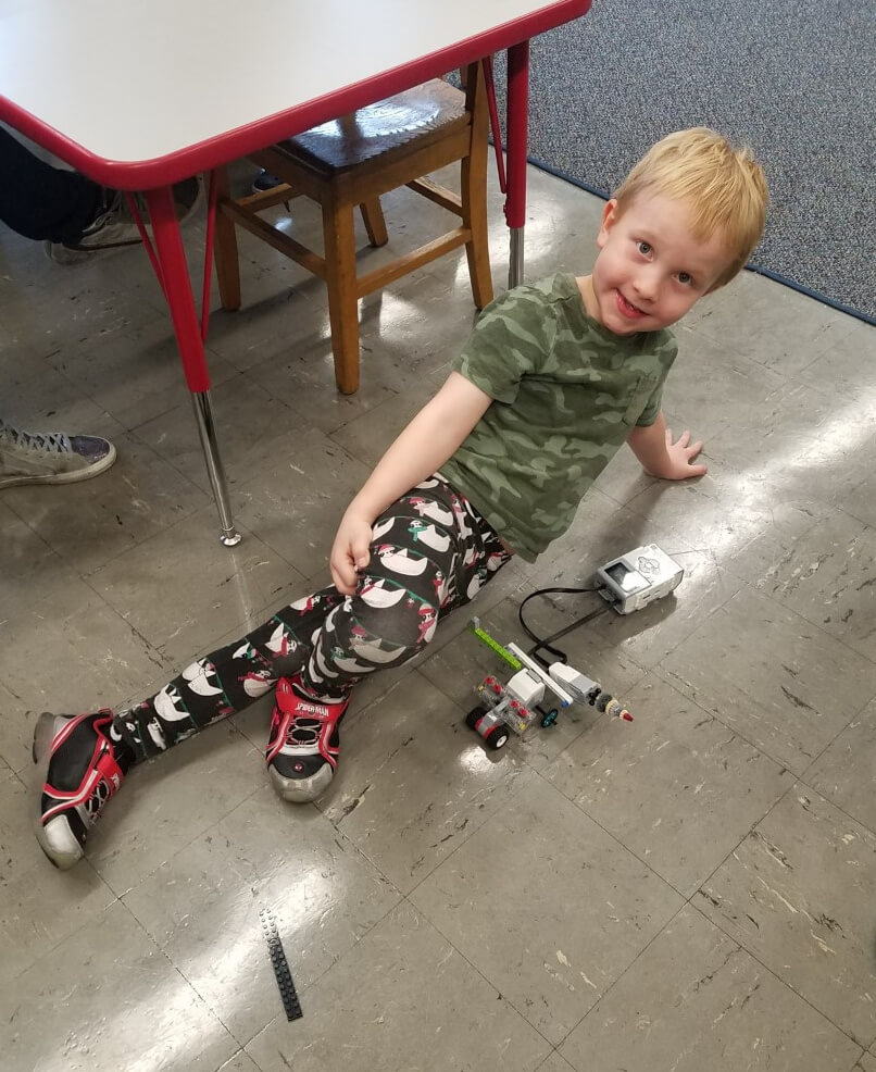 Photo of the author's son on a classroom floor next to a small robot.