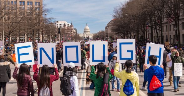 A row of people with their backs to the camera, each holding a sign with one letter of the word "Enough"