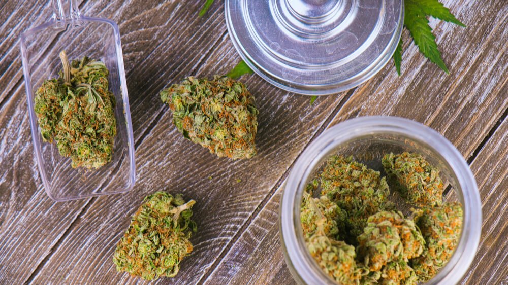 Cannabis in glass jars and spread out on a wooden table.