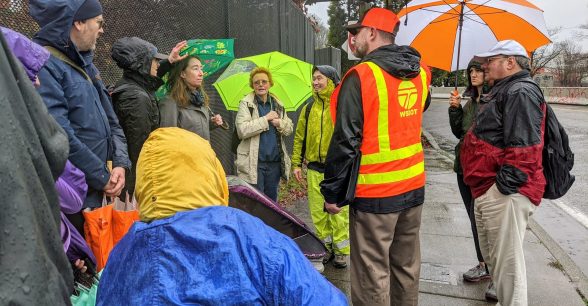 People in the rain on sidewalk with person in orange WSDOT vest