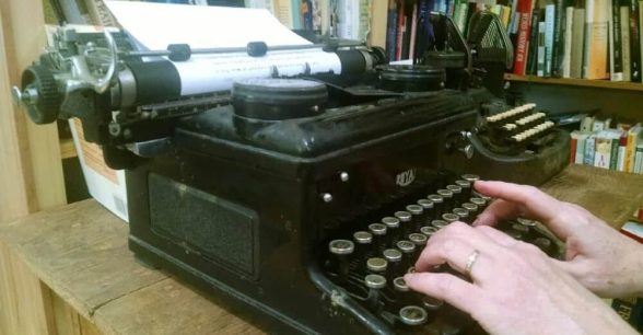 Photo of hands typing on an old black typewriter.