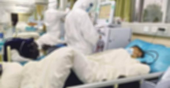 Blurred photo of medical professionals in protective gear treating a patient.