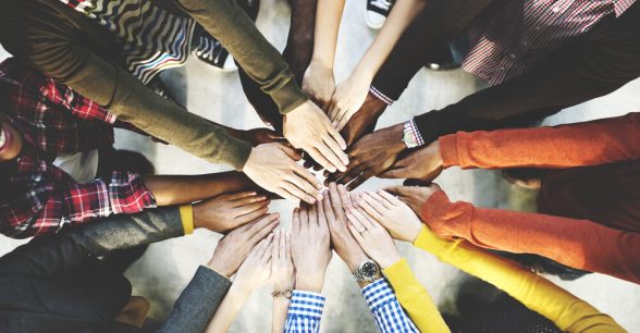 Photo of people of different skin colors standing in a circle, all holding their hands together