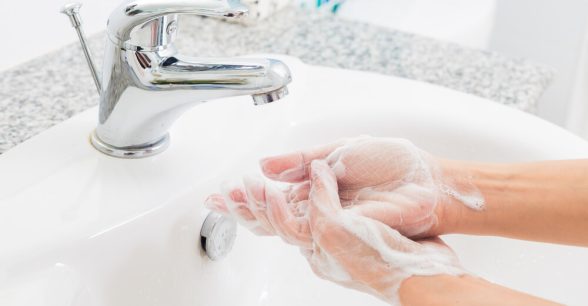 Photo of hands covered in soap under a sink with running water.