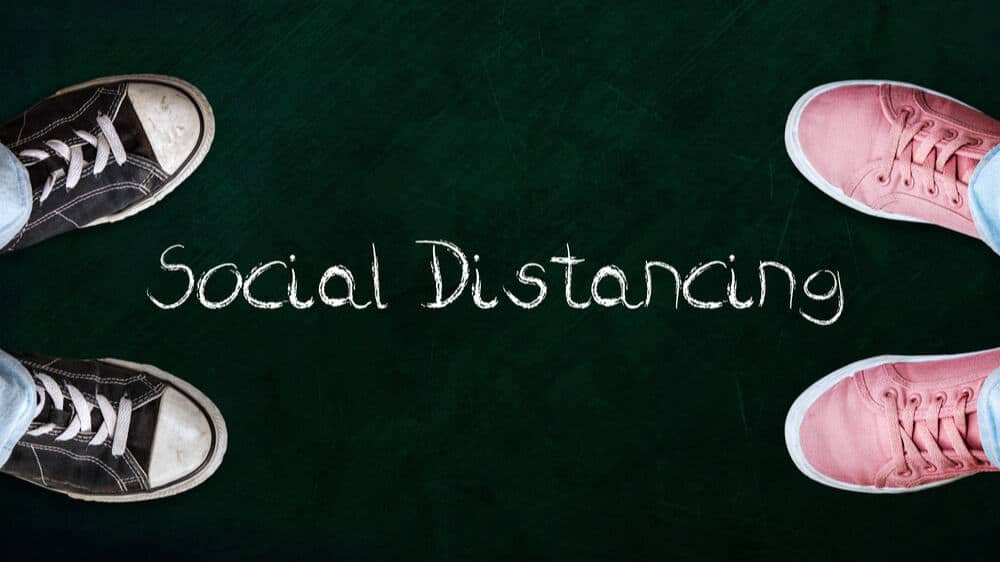 Two people standing on chalkboard with the word social distancing in between.
