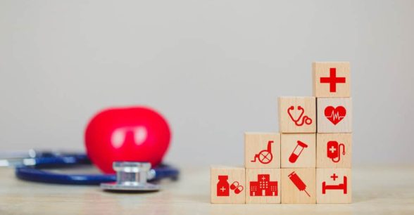 A photo of a stethoscope on a table next to building blocks with medical icons like a stethoscope and hospital bed to indicate building blocks of healthcare.