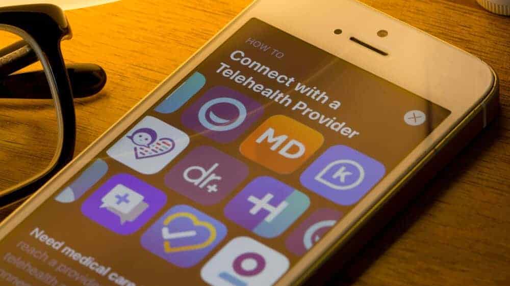 Mobile app icons of assorted telehealth providers from the App Store are seen on a smartphone.