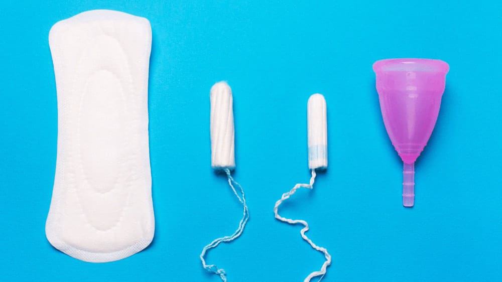 A menstrual pad, two tampons, and a menstrual cup against a bright blue background.